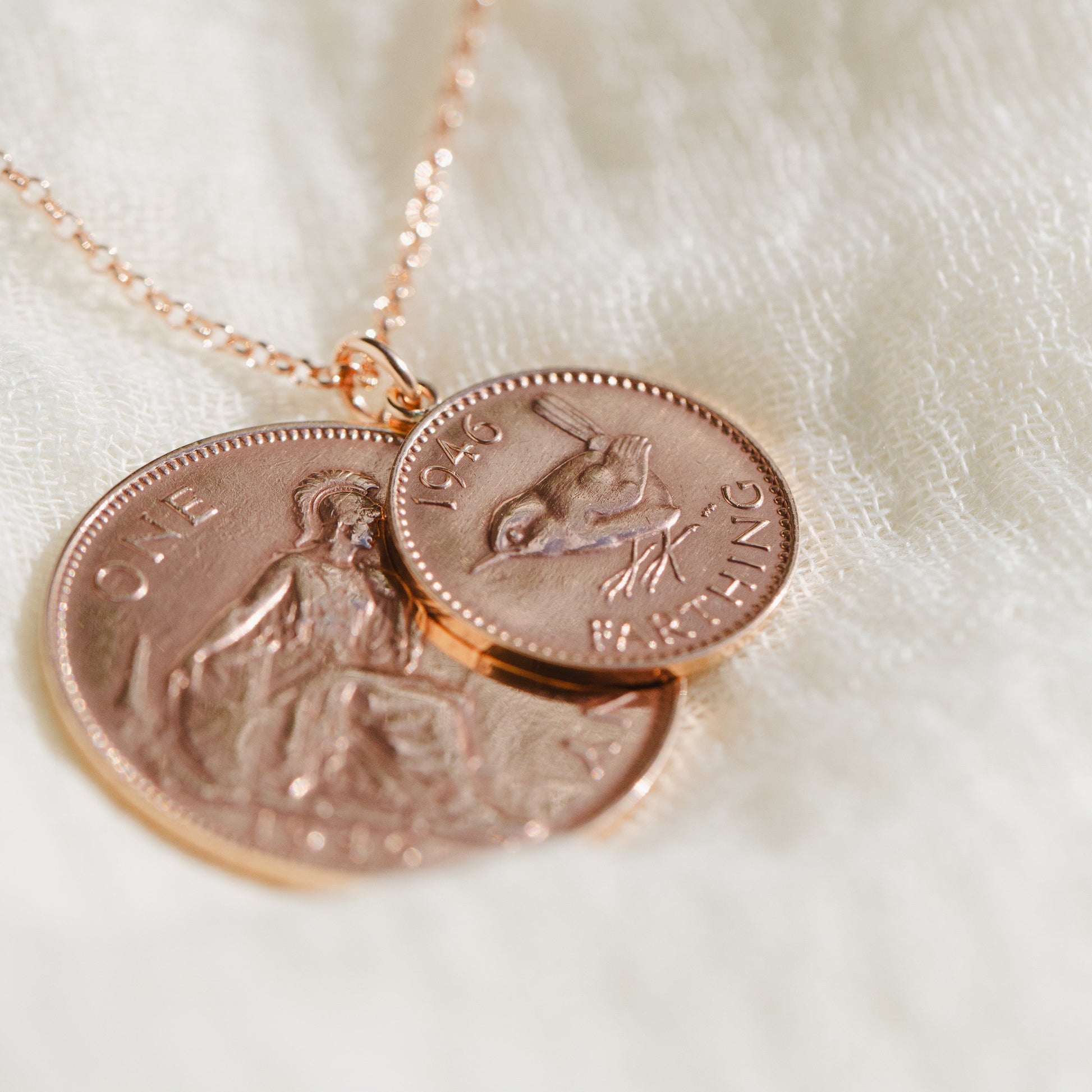 Necklace with a bronze vintage one penny coin and farthing double two coin pendant on a white fabric background.