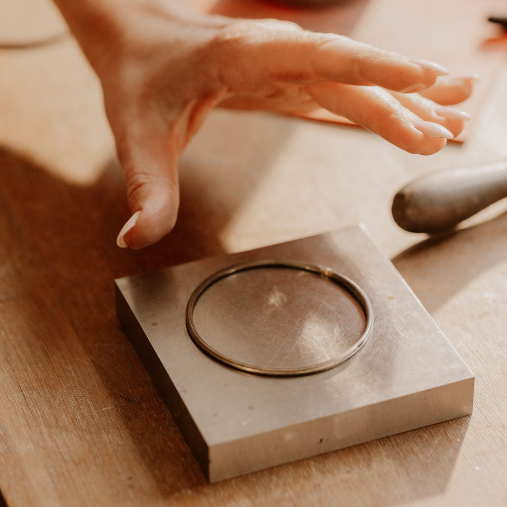 Hand interacting with a Prenoa sterling silver handmade bangle, being placed down ready for hammering flat.