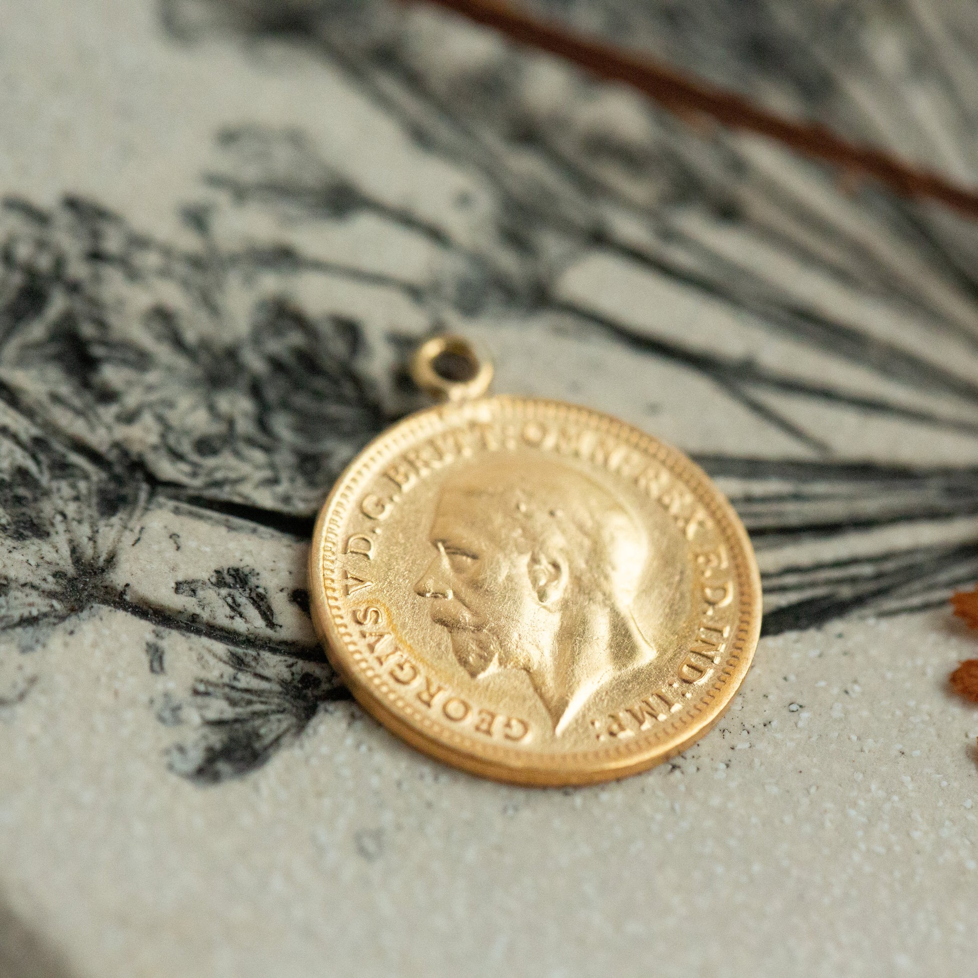 Gold coin pendant on a textured surface with botanical illustrations