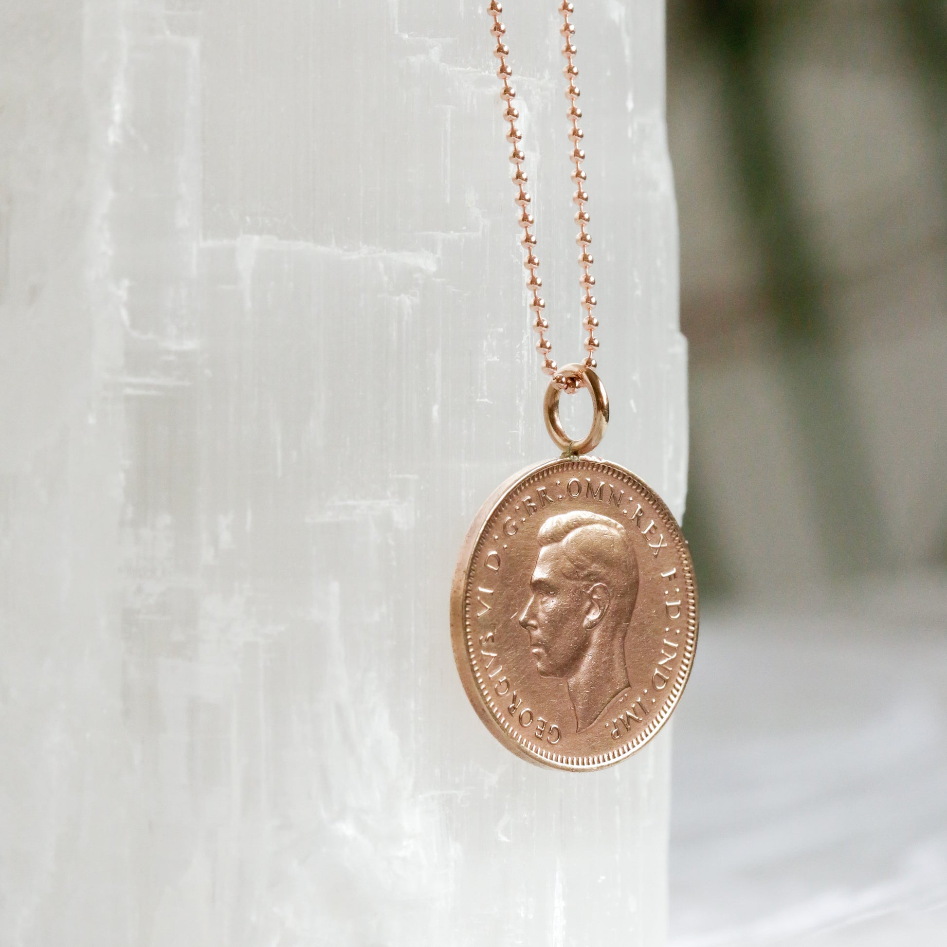 Rose gold chain with bronze farthing coin necklace on a white stone surface