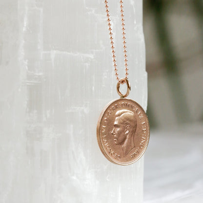 Rose gold chain with bronze farthing coin necklace on a white stone surface