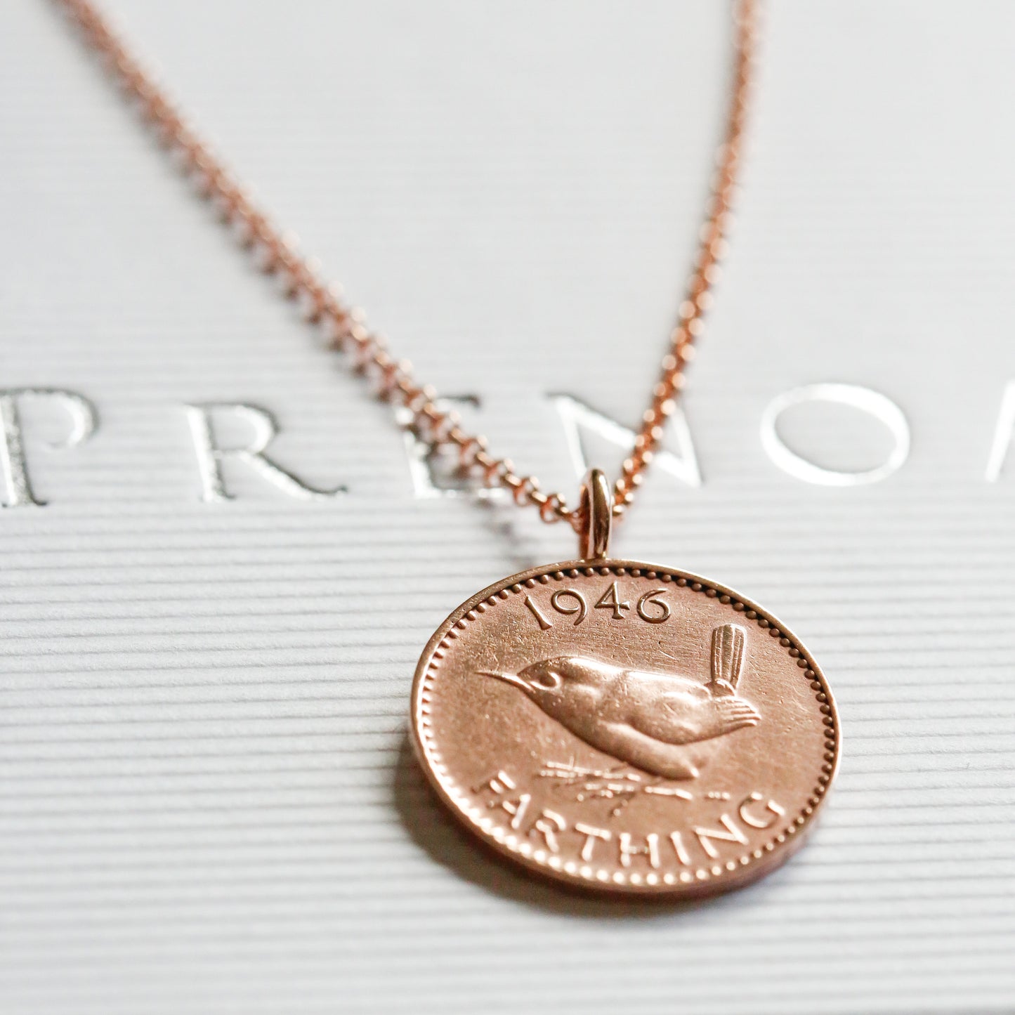 1946 Rose gold necklace with a bronze coin pendant on a white surface