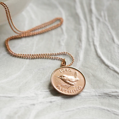 Rose gold necklace with a bronze British farthing coin pendant on a light fabric background