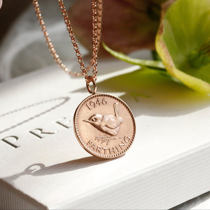 Rose gold necklace with a coin pendant on a white surface with green leaves.