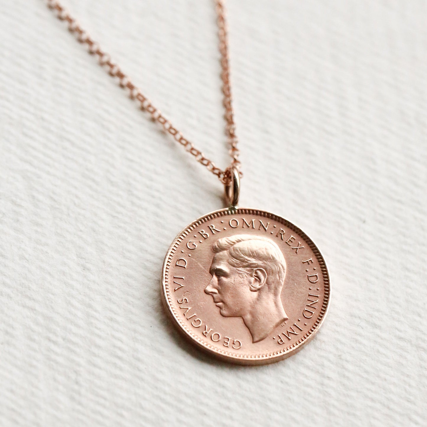Rose gold coin necklace on a white fabric background