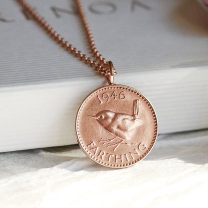 Rose gold necklace with a wren farthing coin pendant on a white surface with a blurred background