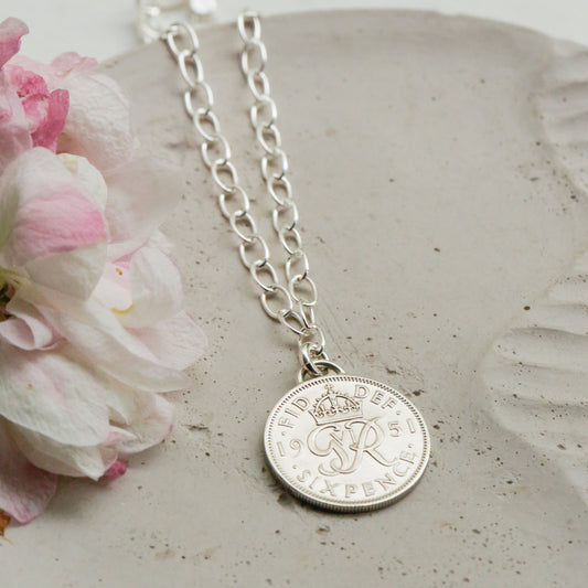 Silver coin necklace with a real round coin pendant on a textured stone surface with flowers. Oval link sterling silver bracelet.