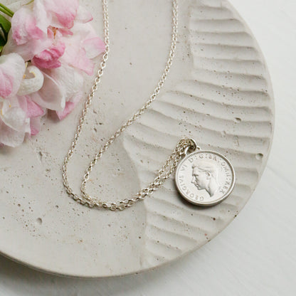 George VI sixpence pendant with sterling silver 1.7mm rolo chain on a cement dish with a floral damson blossom
