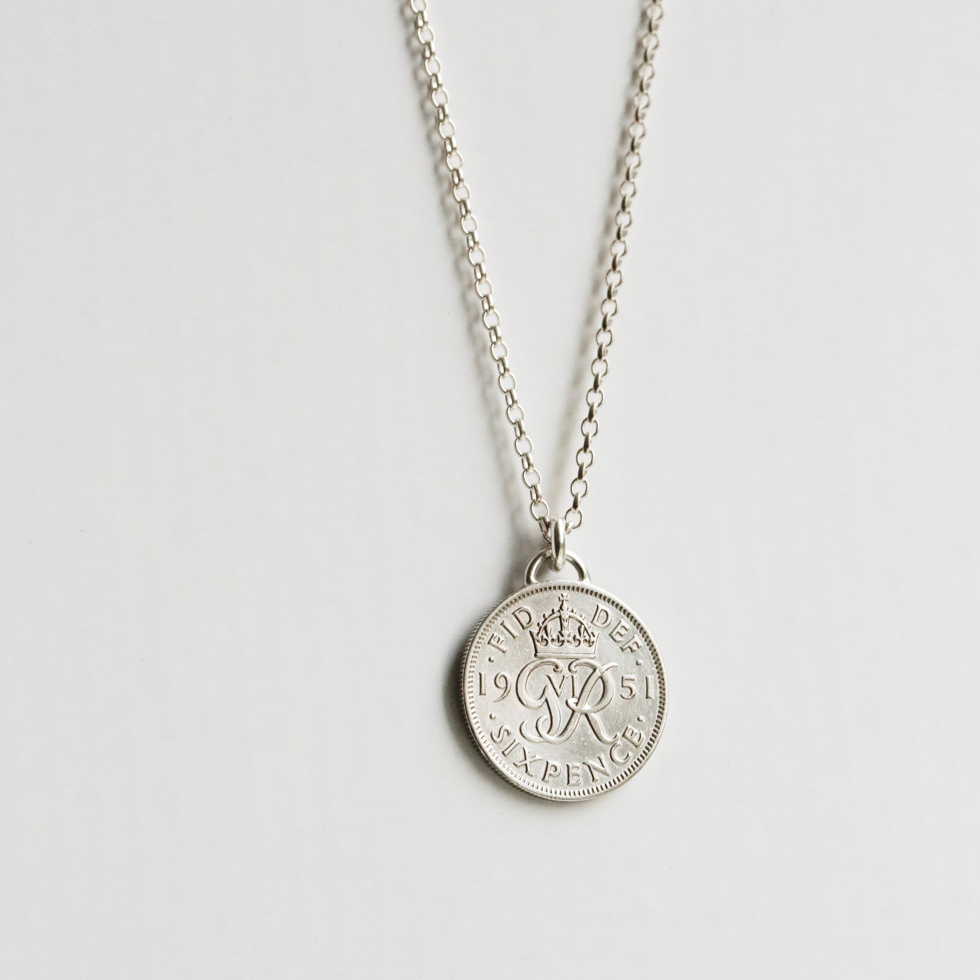 Silver sixpence coin necklace with a round pendant on a light gray background, sterling silver chain hanging down.