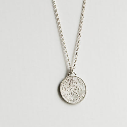 Silver sixpence coin necklace with a round pendant on a light gray background, sterling silver chain hanging down.