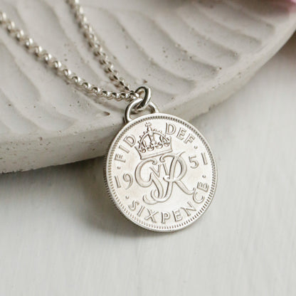 Silver sixpence necklace with a round pendant on a white surface with flowers
