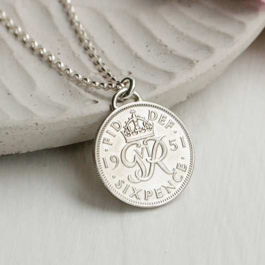 Silver sixpence necklace with a round pendant on a white surface with flowers