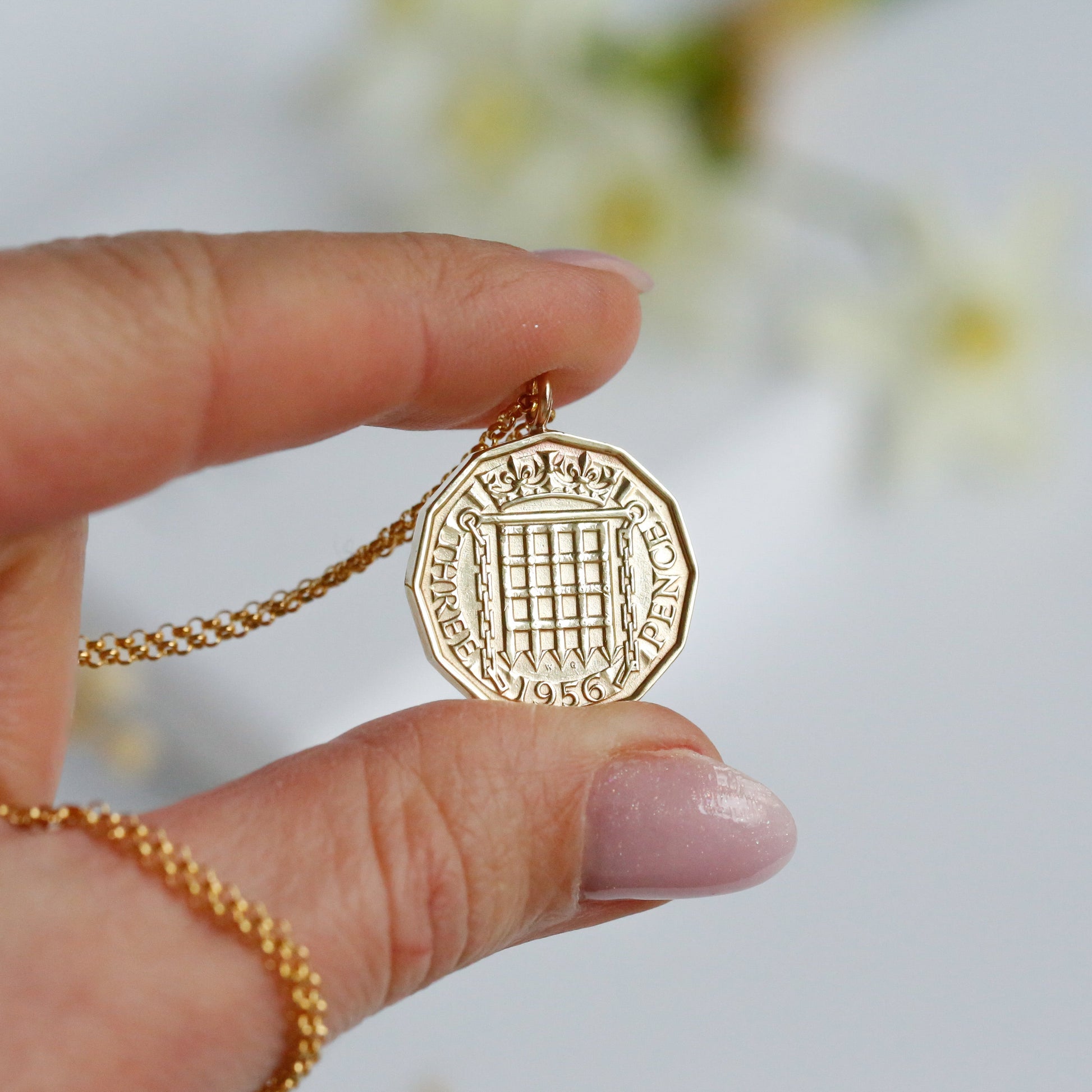 Gold coin necklace with 1956 brass British threepence coin, being held in a hand with a white  background. 70th birthday coin jewellery. 