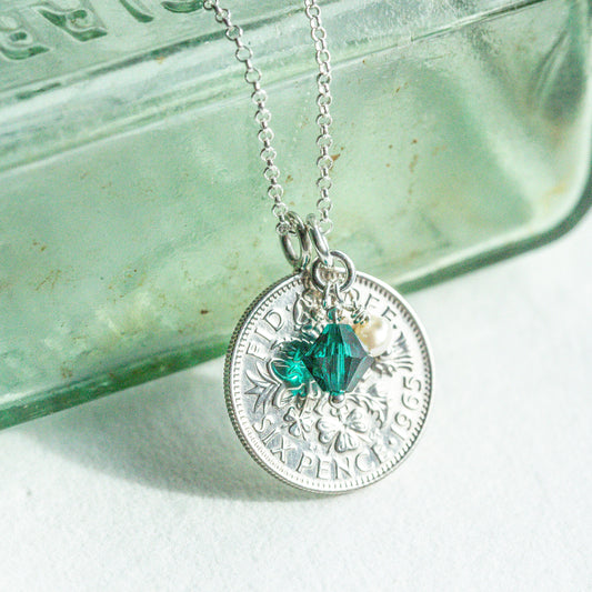 Silver sixpence coin necklace with a green gemstone pendant on a light background