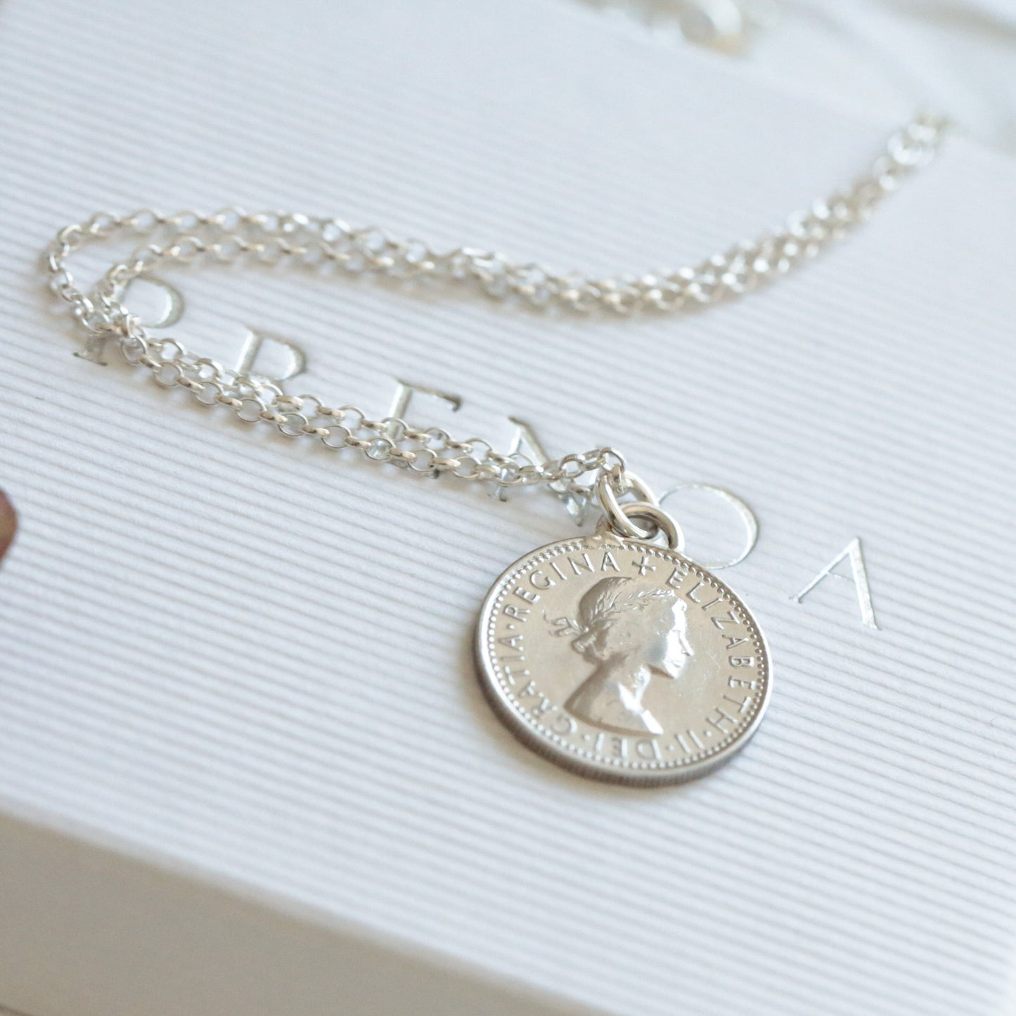Silver sixpence coin necklace with a coin pendant on a white surface with flowers in the background