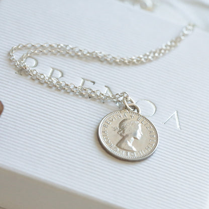 Silver sixpence coin necklace with a coin pendant on a white surface with flowers in the background