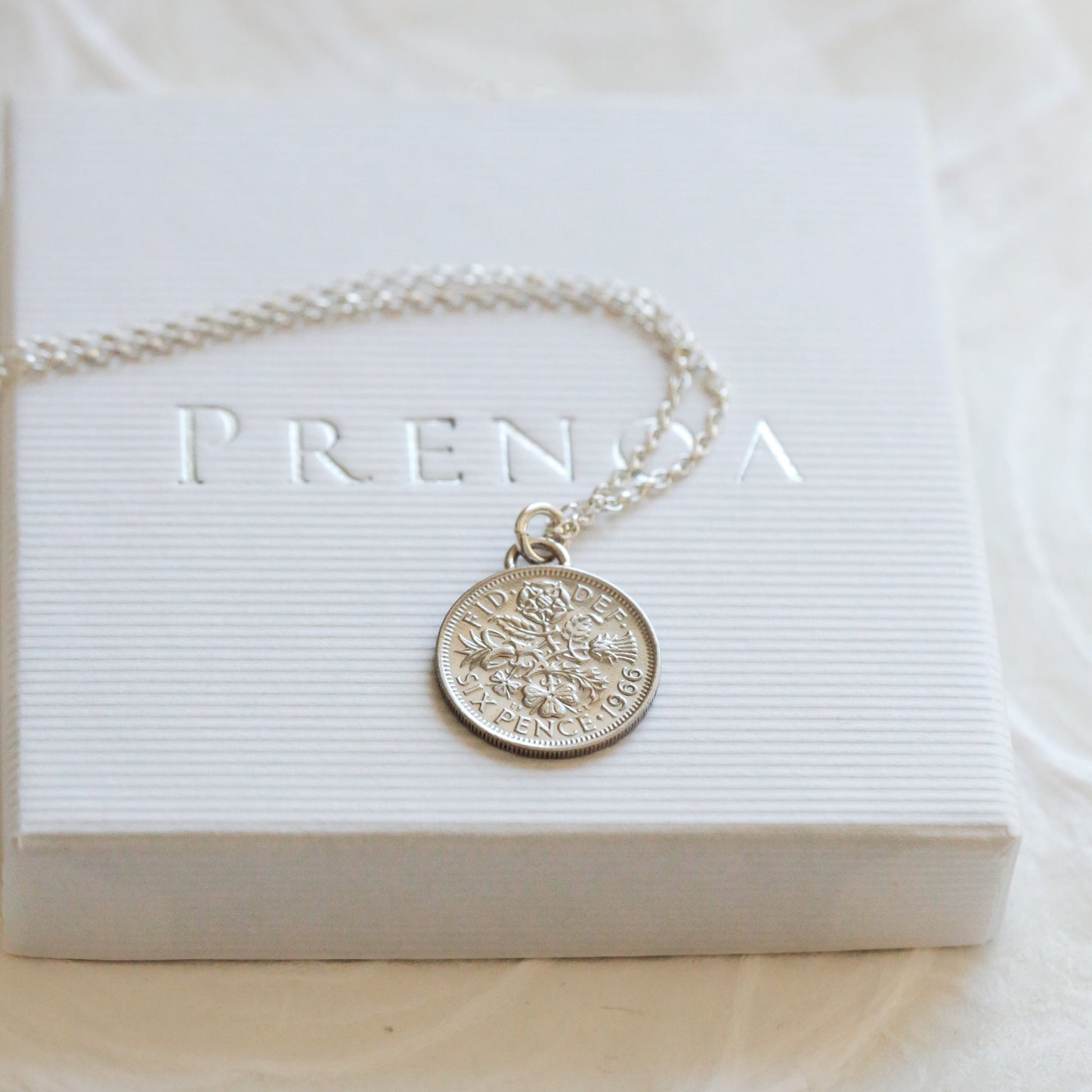Silver coin necklace with a round pendant on a white box with 'PRENDA' branding.