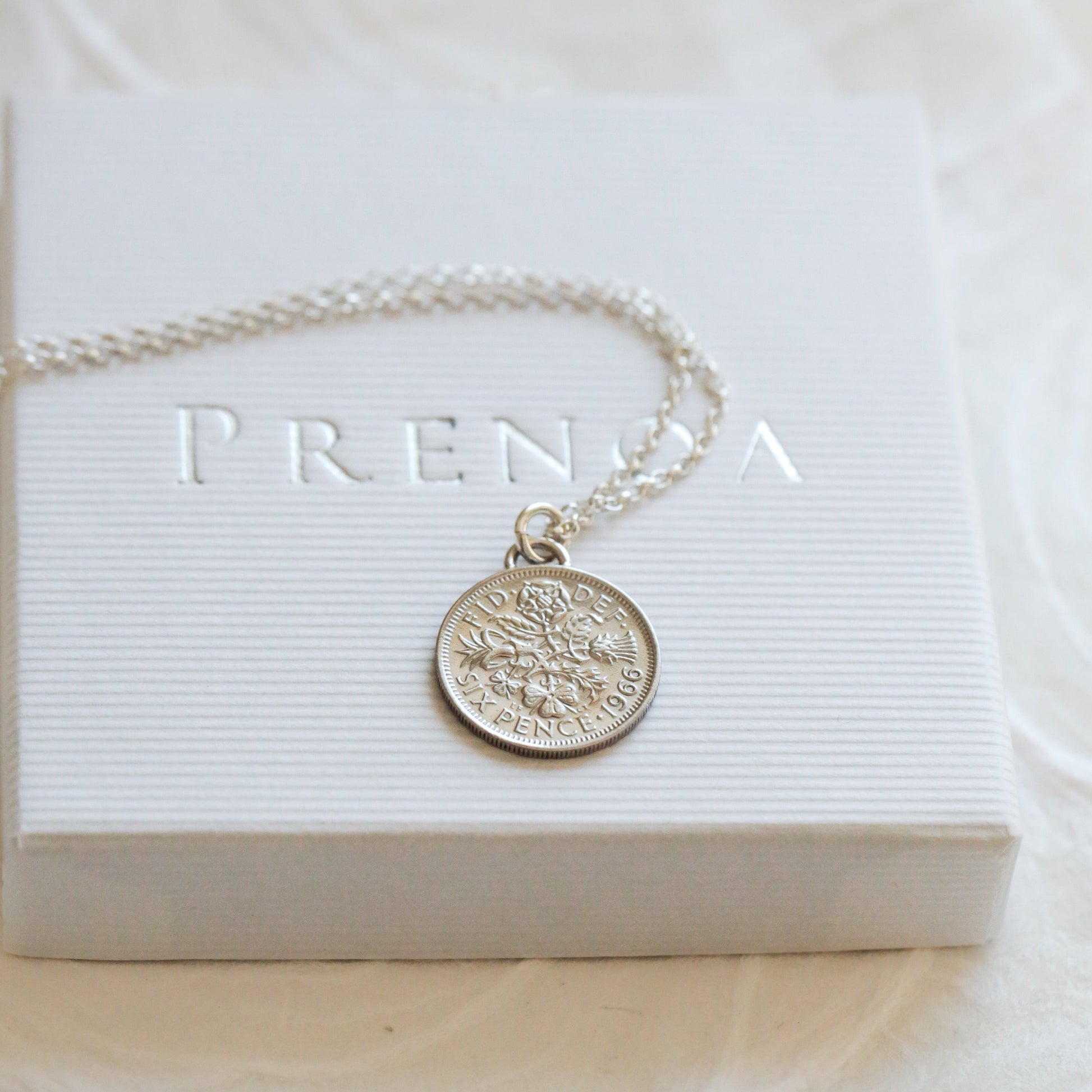 Silver coin necklace with a round pendant on a white box with 'PRENDA' branding.