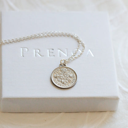 Silver coin necklace with a round pendant on a white box with 'PRENDA' branding.