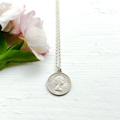 Silver coin necklace on a white surface with pink flowers