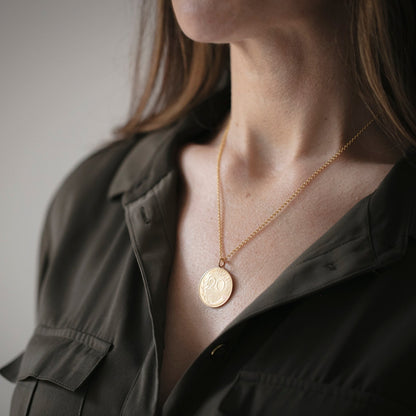 Person wearing a gold necklace with a coin pendant against a neutral background
