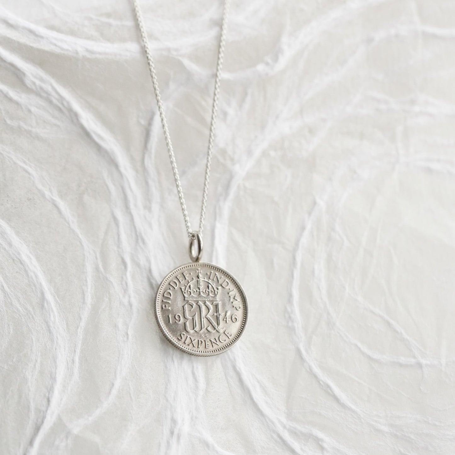 1946 Silver British sixpence necklace with a round pendant on a white textured fabric background