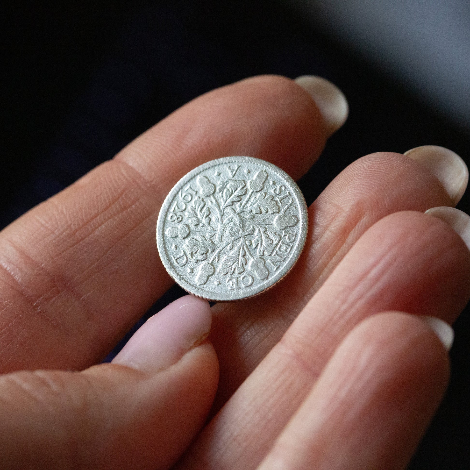 Hand holding a half silver sixpence pin badge, inspecting the patina of the coin.