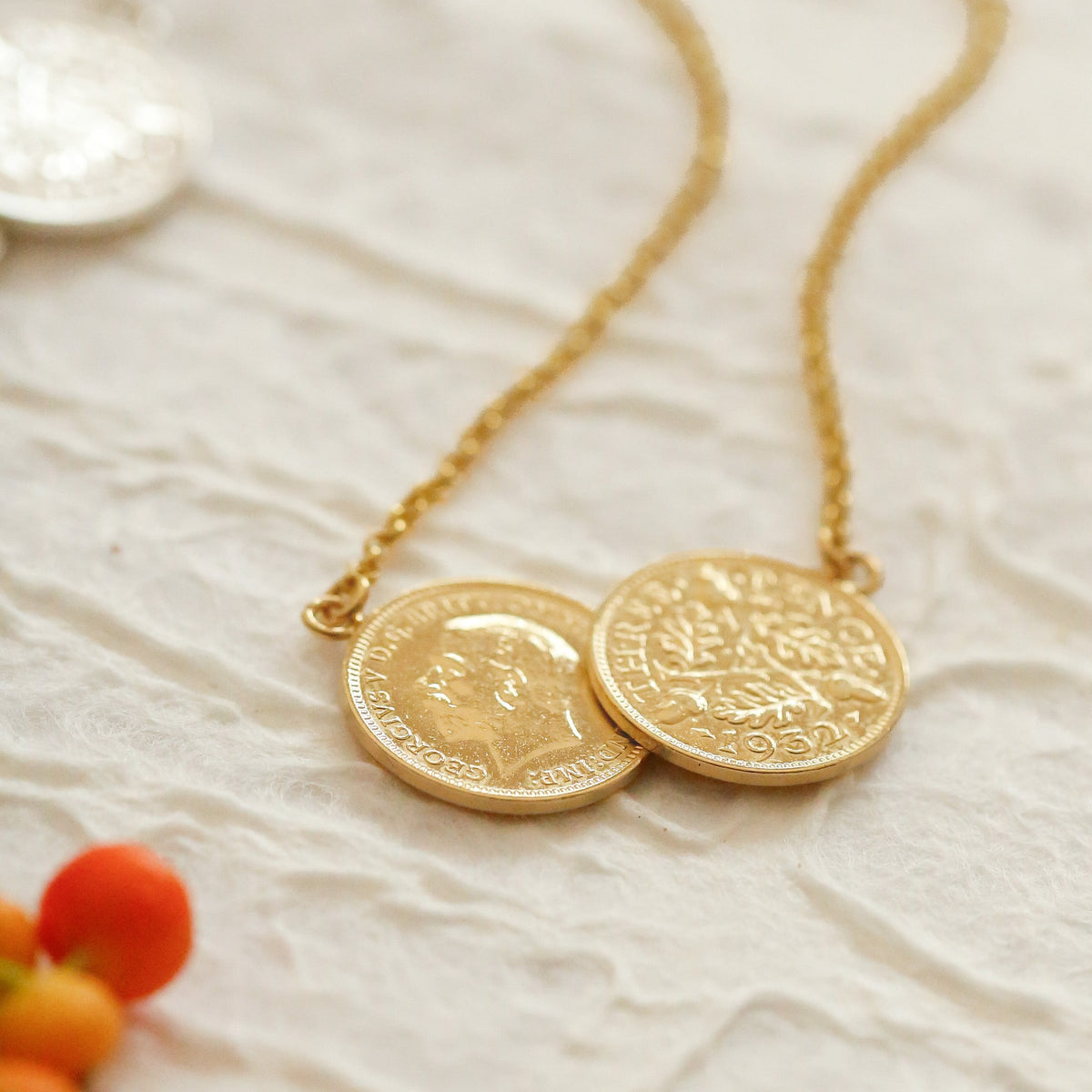 Double gold threepence necklace laid down on a white paper background with orange berries