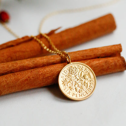 Gold sixpence necklace on white background resting on cinnamon