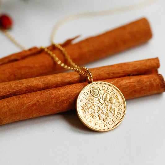 Gold sixpence necklace on white background resting on cinnamon