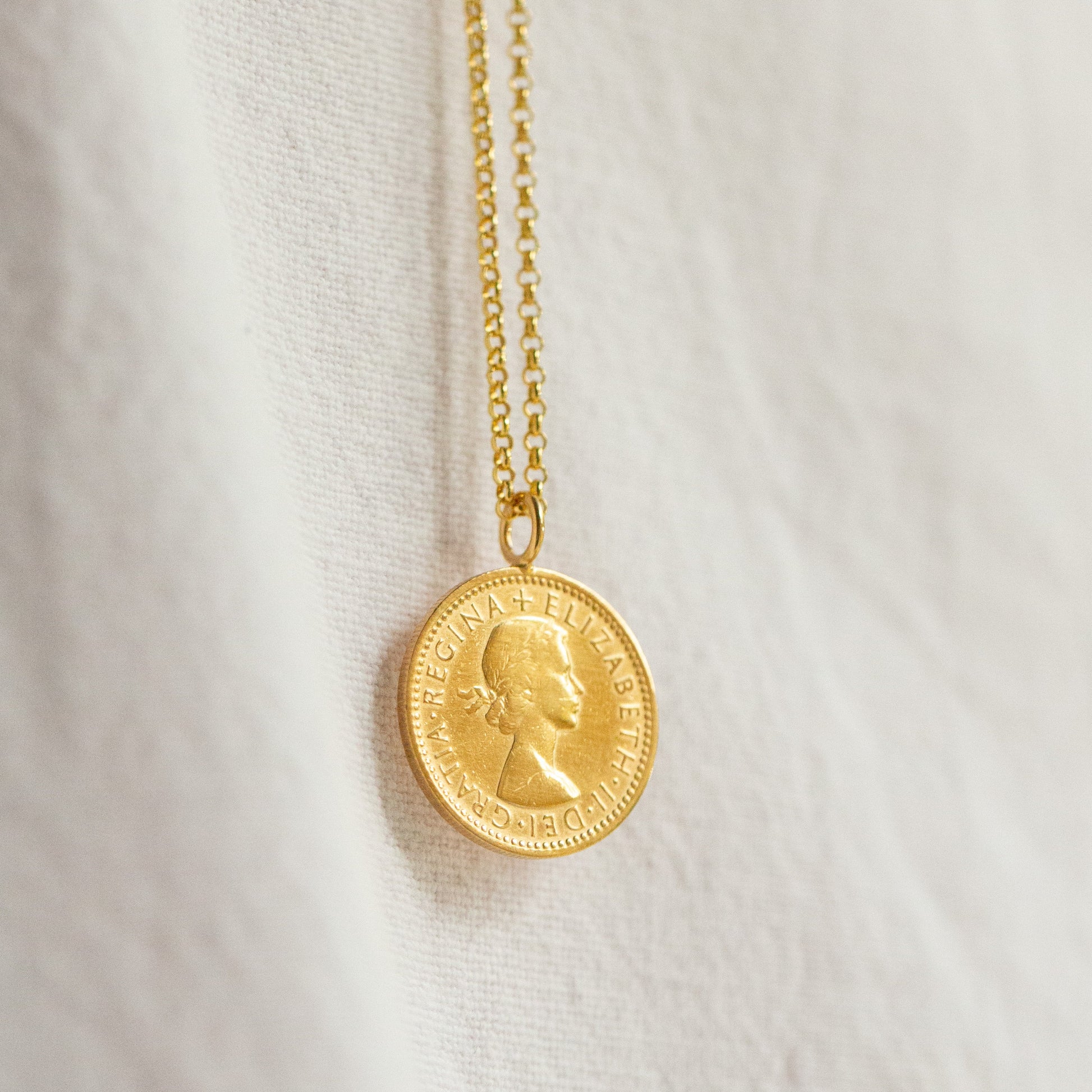 Gold necklace with a coin pendant on a white fabric background