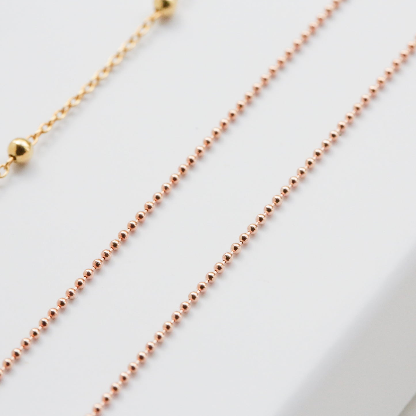 Two gold necklaces on a white surface