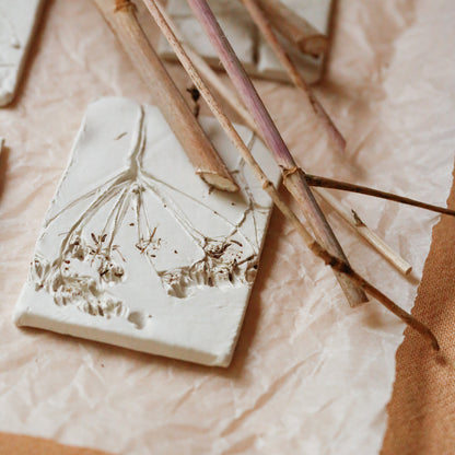 A close-up of the botanical embossed dried floral keepsake, placed on crumpled white paper with dried stems and warm tan fabric around it.