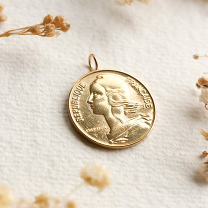 Gold French coin pendant with a profile design on a light background with dried flowers