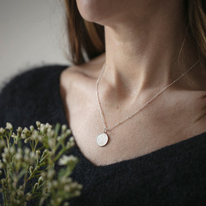 Person wearing a delicate bee coin necklace with a small pendant, holding a bouquet of flowers.