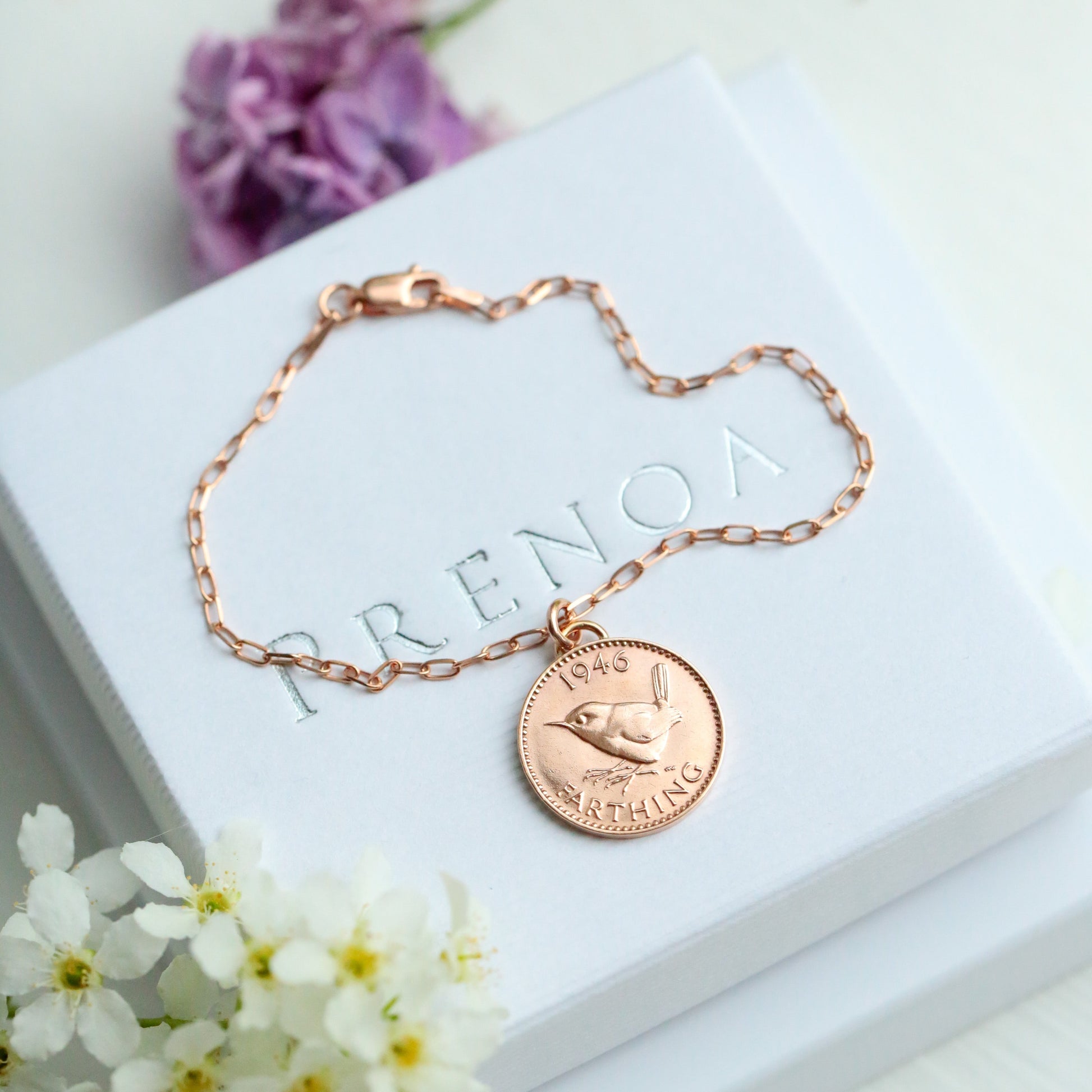 Rose gold bracelet with a 1946 farthing coin charm on a white box with flowers around
