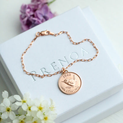 Rose gold bracelet with a 1946 farthing coin charm on a white box with flowers around