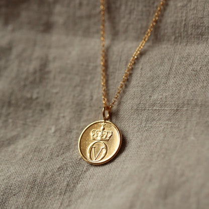 Gold coin necklace with a round bee pendant see with 22ct gold and a gold vermeil chain, on a textured fabric background