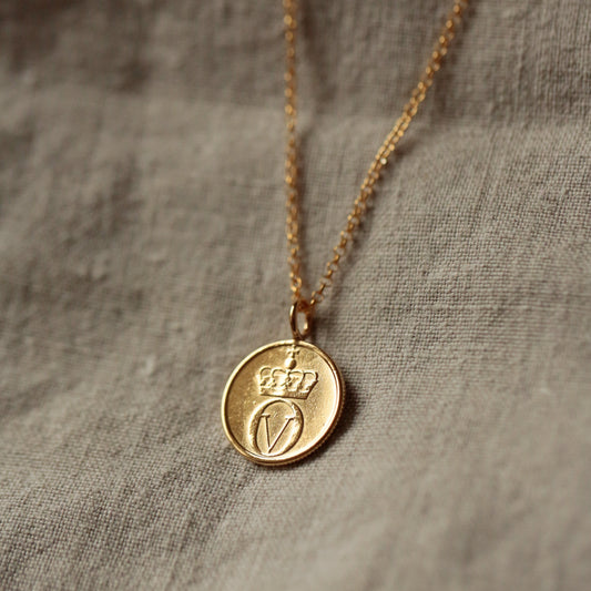 Gold coin necklace with a round bee pendant see with 22ct gold and a gold vermeil chain, on a textured fabric background