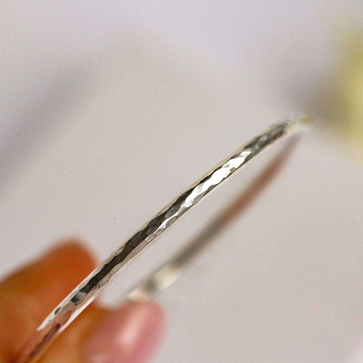 Silver bangle held by a hand with a blurred background