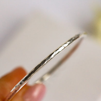 Silver bangle held by a hand with a blurred background