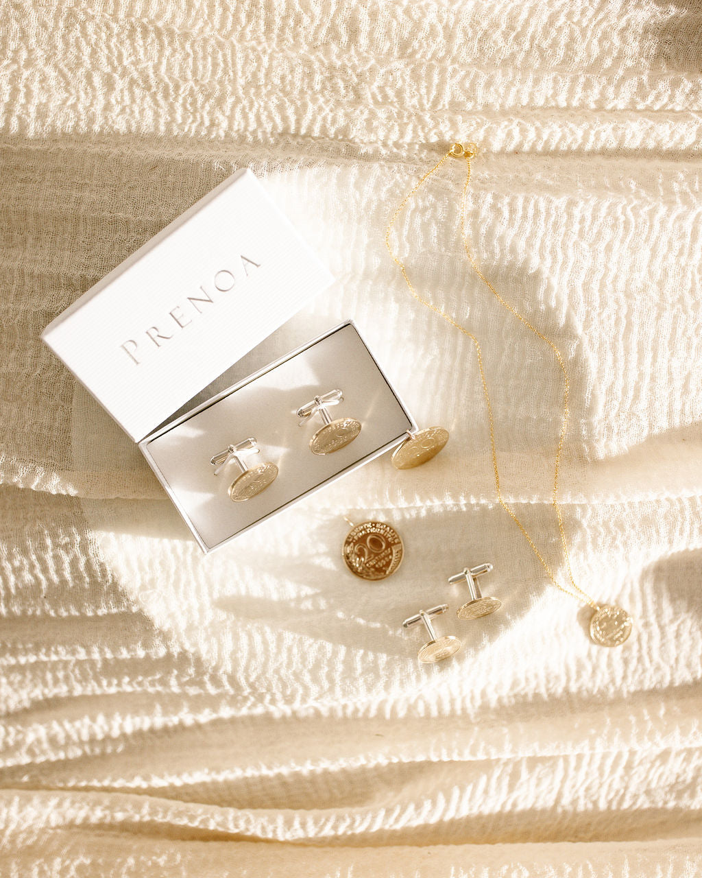 Heirloom silver and gold coin jewellery set including earrings, cufflinks and a necklace on a textured beige surface with Prenoa branding. Classic real coin jewellery made in Stamford UK using real coins and precious metals. Ideal for 60th, 70th, 80th and 90th birthday gifts, bridal gifts, weddings, anniversaries and Christenings.