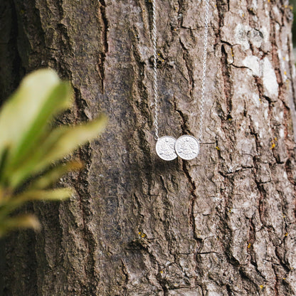 A necklace of two threepence British coins fixed together hangs from an oak tree.