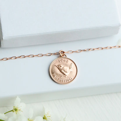 Rose gold necklace with a coin pendant on a white box with 'PRENOT' branding, surrounded by white flowers.
