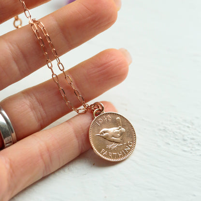 Rose gold necklace with a British farthing coin pendant held by a hand on a light background