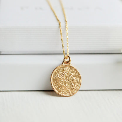 Gold British sixpence necklace with a gold chain on a white surface