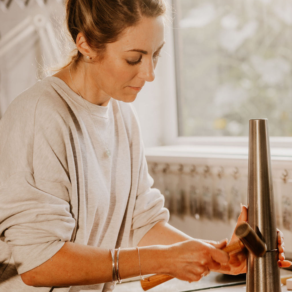Our Founder Becky working on a sterling silver bangle with a hammer in a workshop creating a circular bangle 