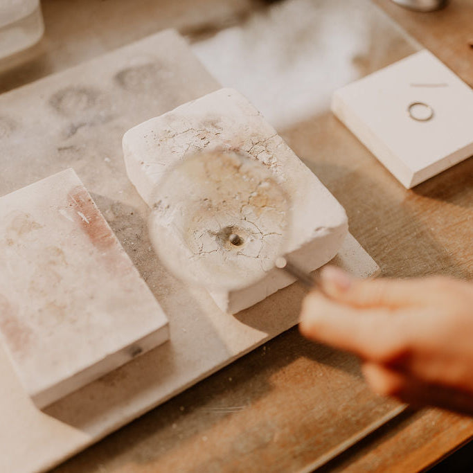 Close-up of a hand holding a small stone object on a wooden surface with sterling silver items.
