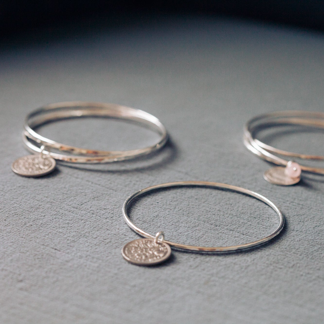 Three silver bangles with circular charms on a gray surface
