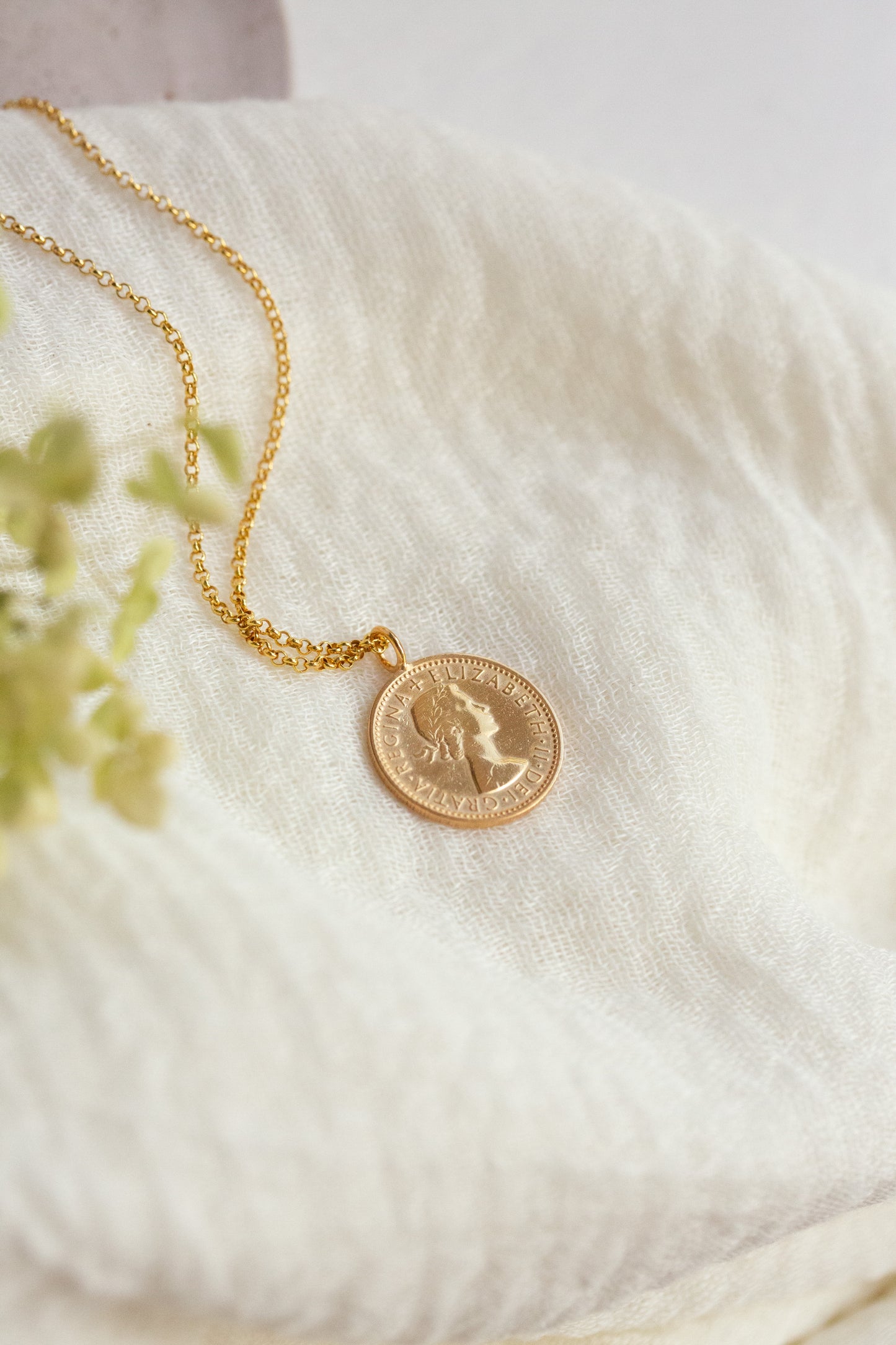 Gold necklace with a coin pendant on a soft white fabric background